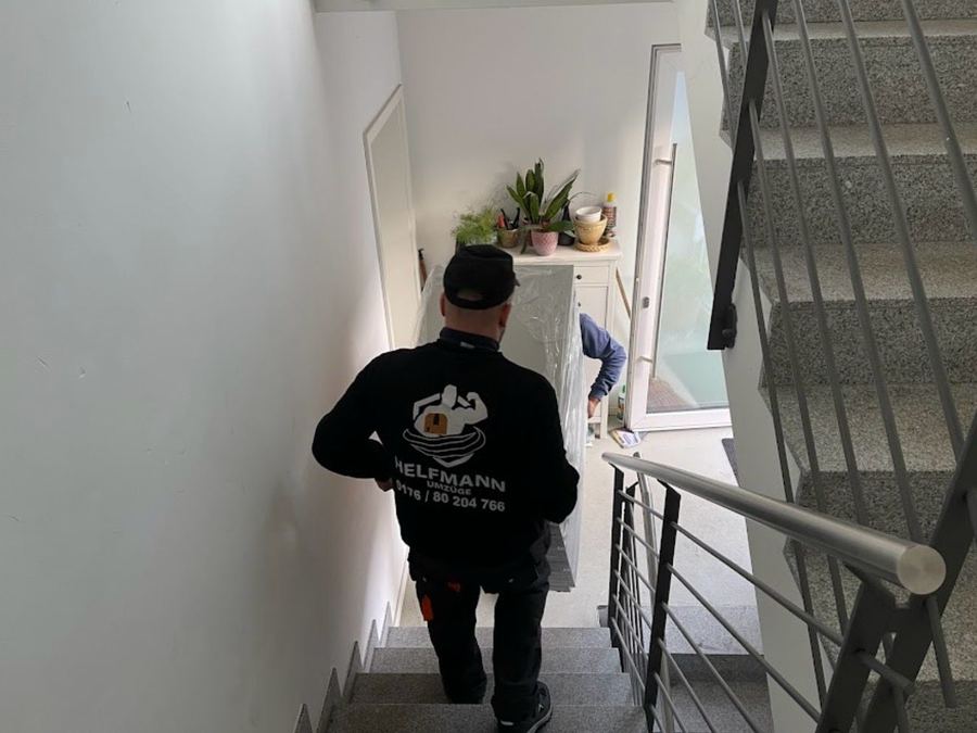 Mitarbeiter von Helfmann Umzüge trägt einen verpackten Schrank durch ein Treppenhaus